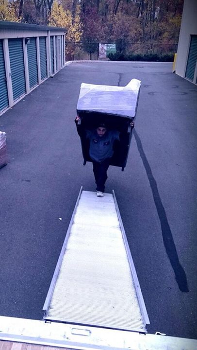 A man is carrying a big piece of furniture to the All Jersey Movers van